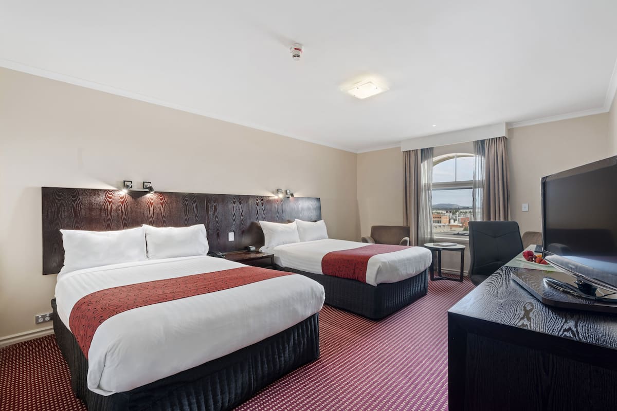 A hotel room with two beds, a desk with a television, a chair, and a window with a view.