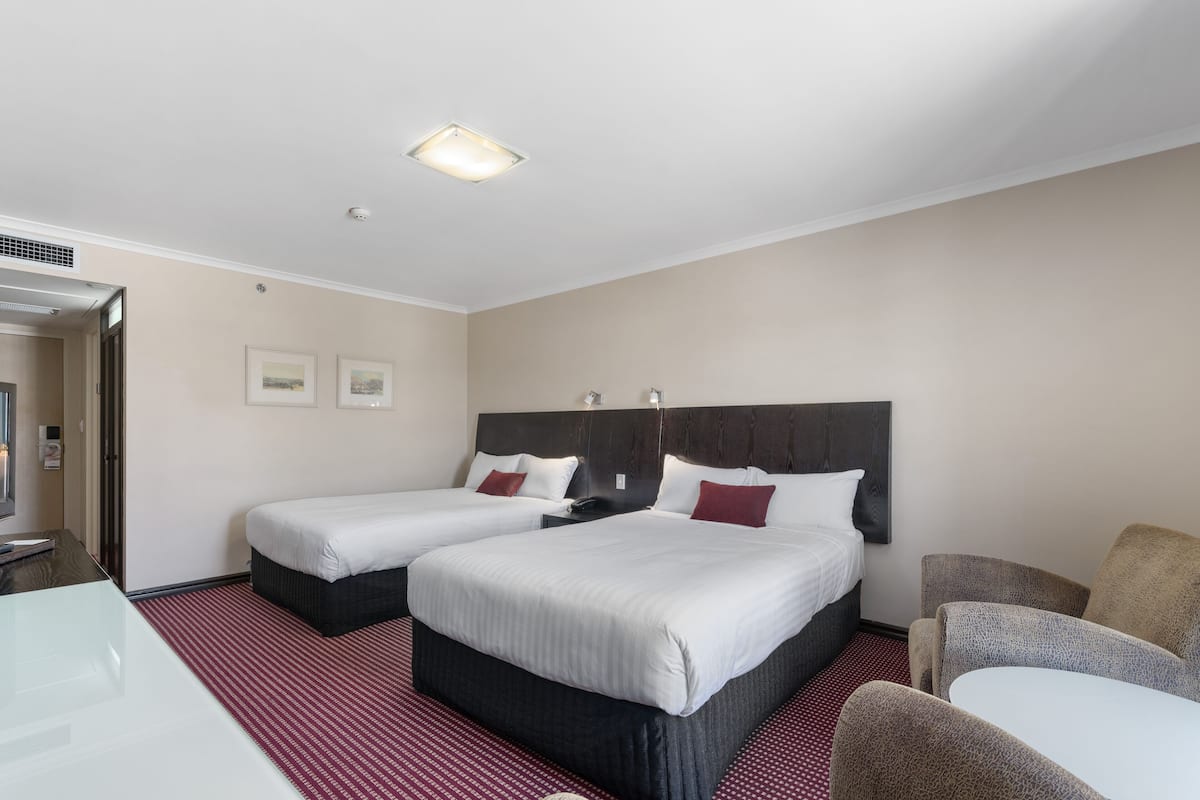 A hotel room with two beds, a desk, and a chair.