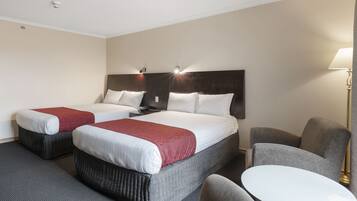 A hotel room with two beds, a desk, a chair, and a lamp.
