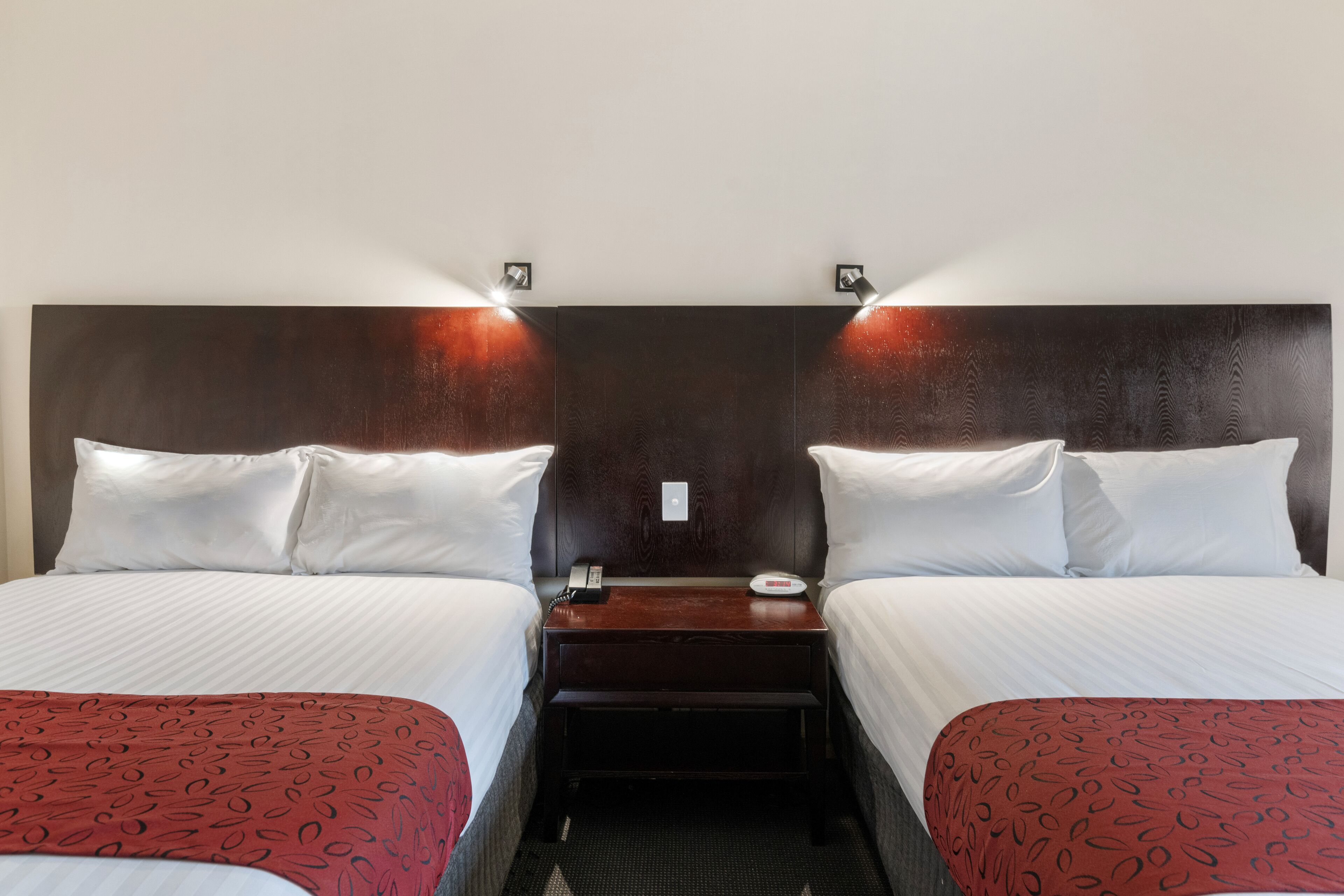 A hotel room with two beds, a wooden headboard, bedside tables with lamps, and a telephone.