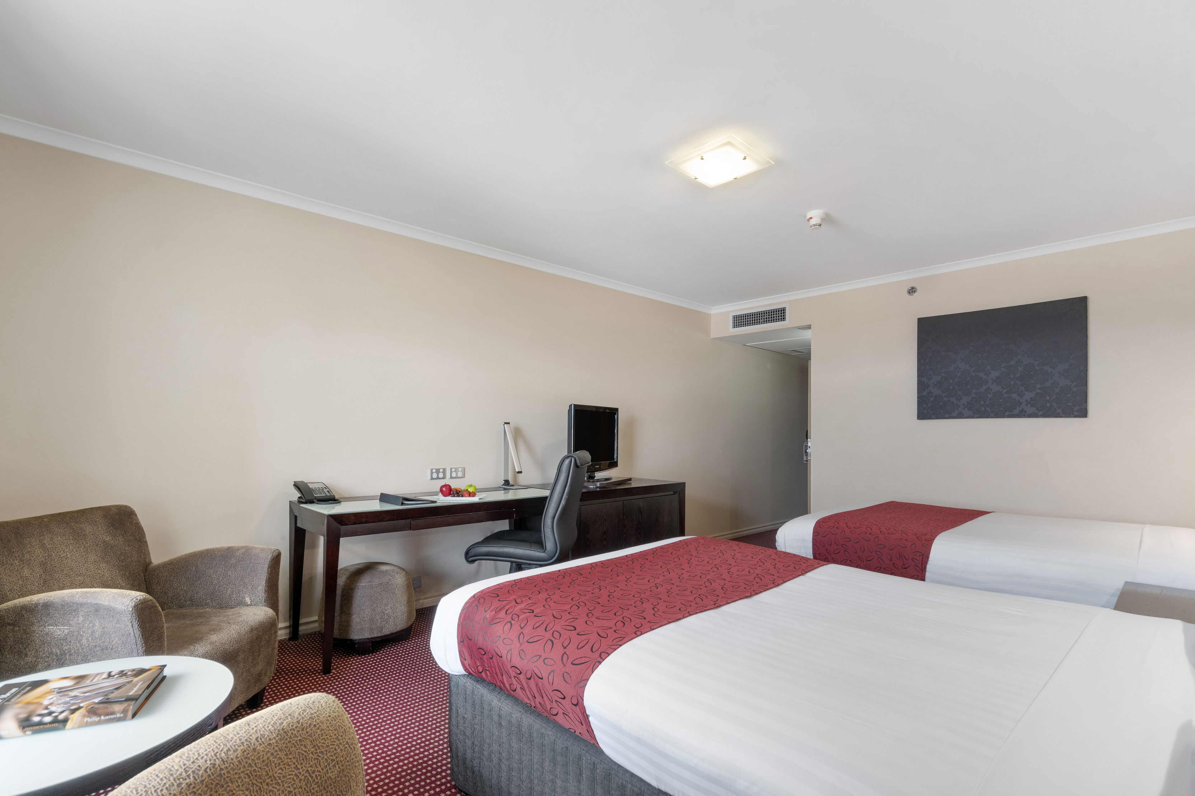 A hotel room with two beds, a desk with a computer, a chair, and a small table with a magazine.