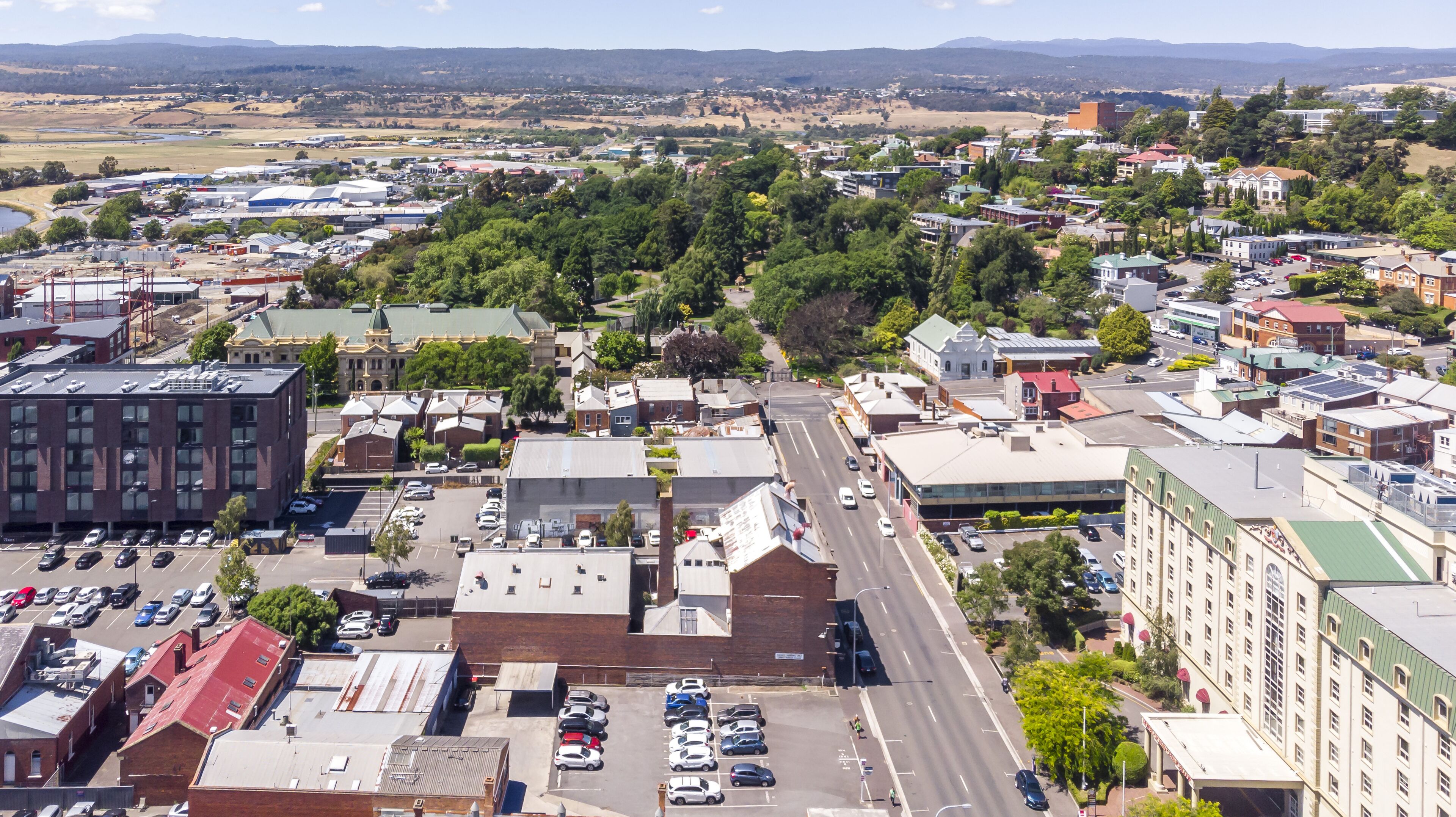 Vista aérea de un pueblo con edificios comerciales y residenciales, una calle principal con coches, y un amplio espacio abierto a lo lejos.