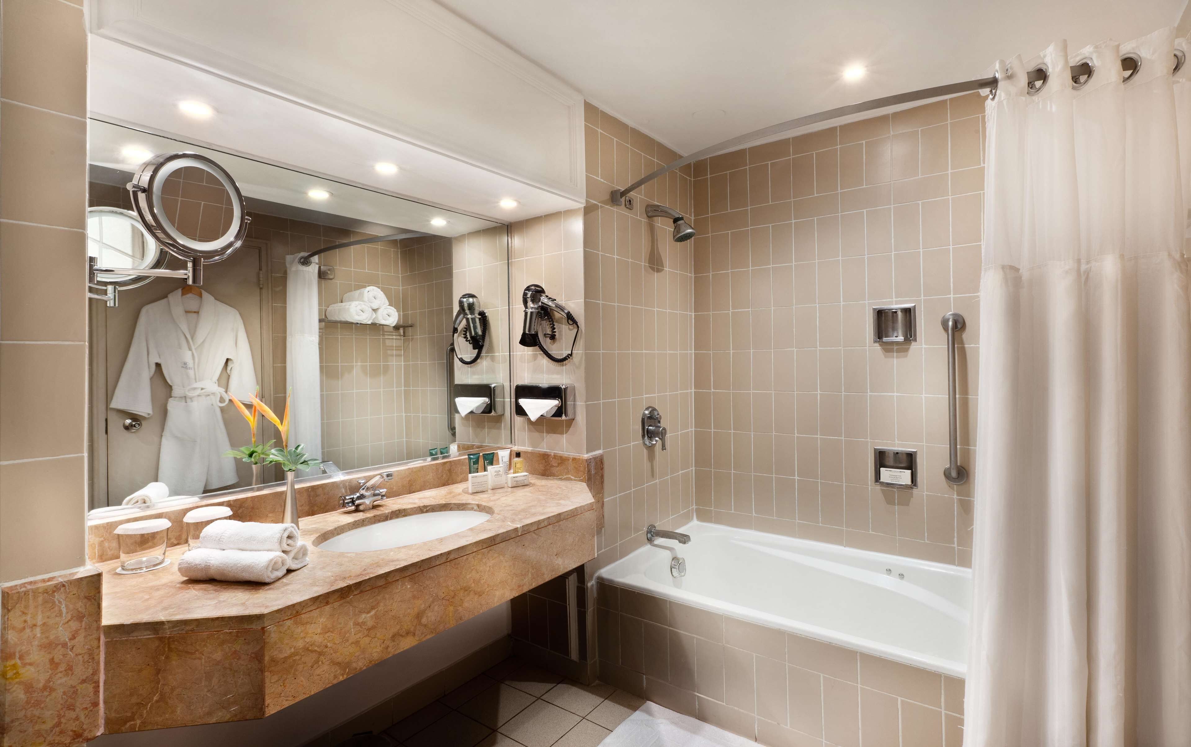 A modern bathroom with a large mirror, a bathtub, a shower, and a vanity with a sink and towel rack.