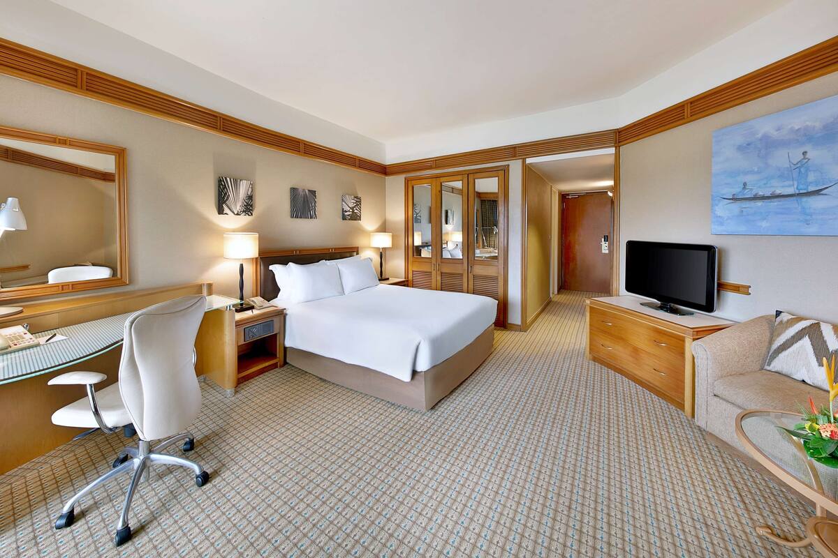 A hotel room with a bed, desk, chair, TV, and a painting on the wall.