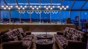 Un coin bar avec vue sur la ville, deux canapés et une table avec une bouteille.