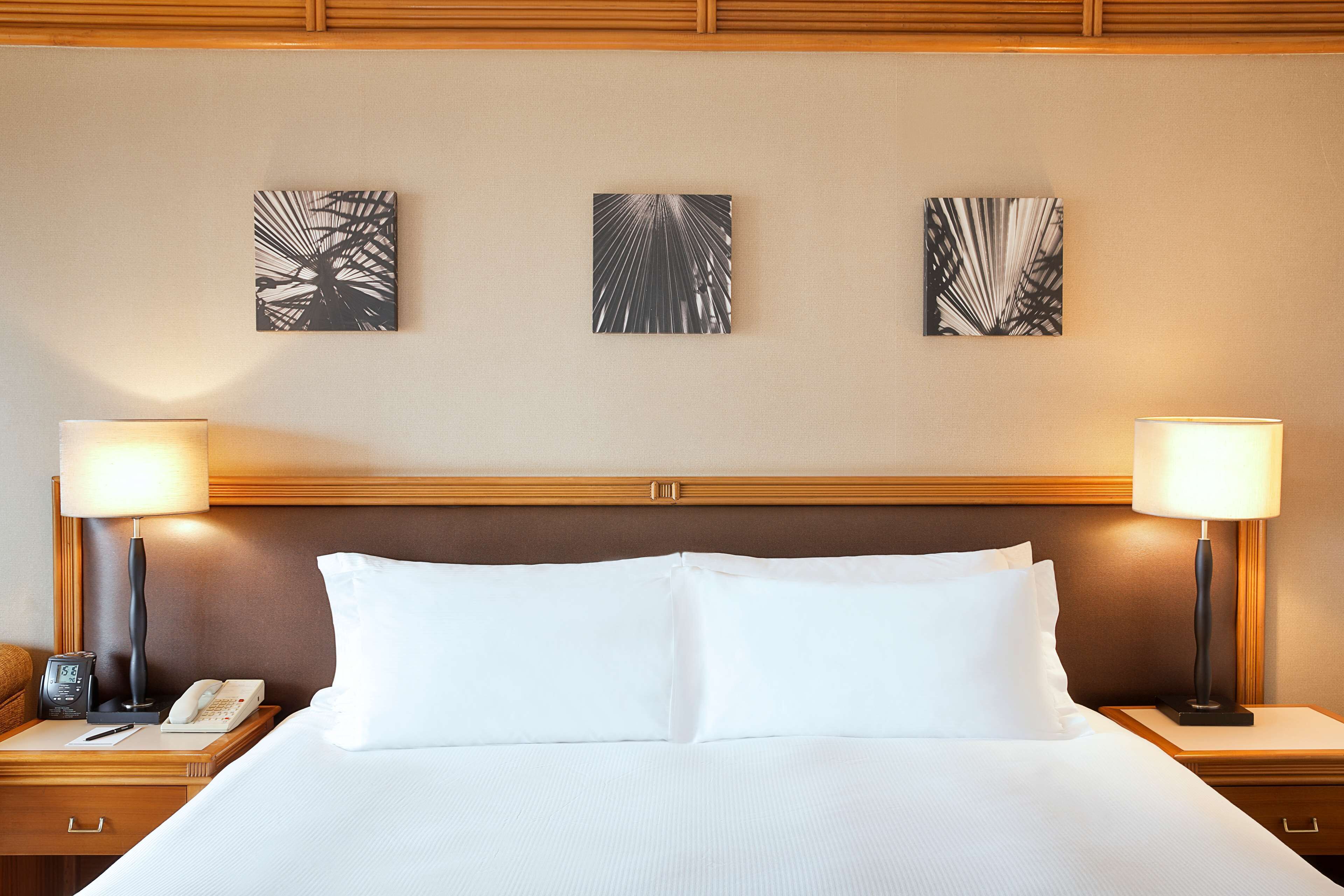 A hotel room with a large bed, two bedside tables with lamps, a phone, and three abstract wall art pieces.