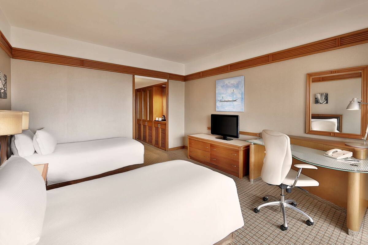 A hotel room with two beds, a desk with a computer, a chair, a telephone, and a mirror.