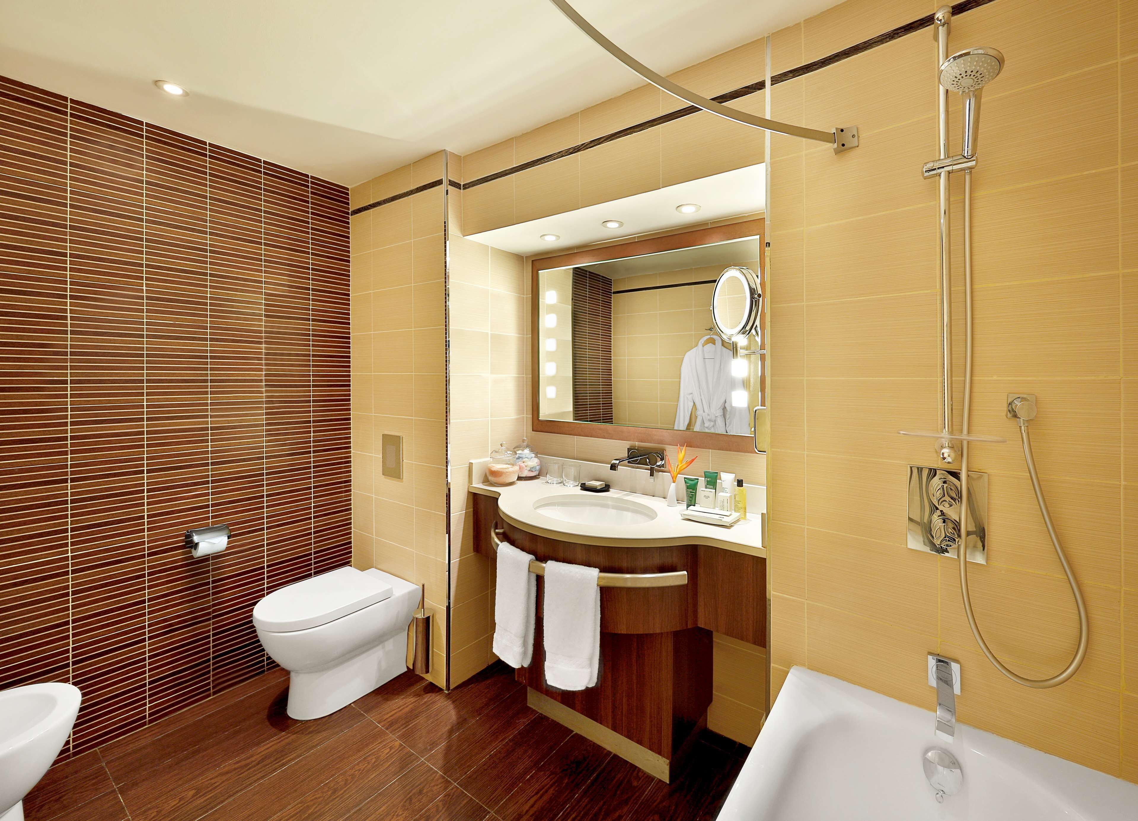 Une salle de bain moderne équipée de toilettes, d’un lavabo et d’une baignoire, avec un lambris en bois et un grand miroir.