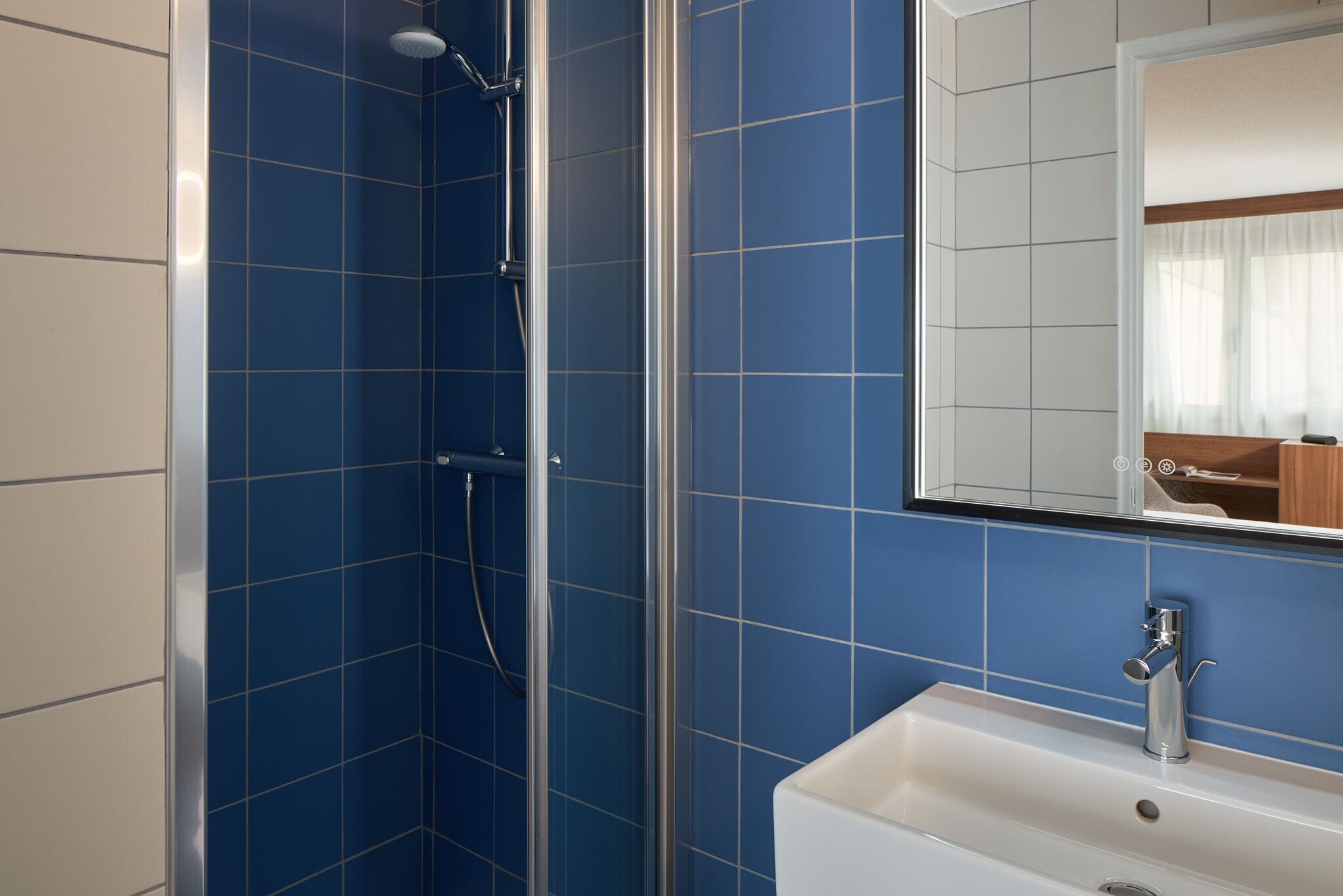Un baño con azulejos azules, ducha y lavamanos con espejo.
