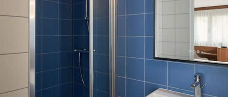 Un baño con azulejos azules, ducha y lavamanos con espejo.