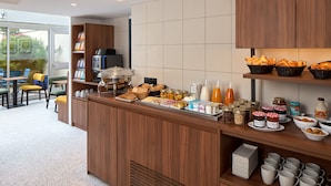 Una barra de desayuno con diversas opciones de comida, una máquina de café y vistas al exterior.