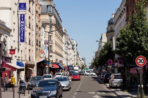 Une rue animée, avec un bâtiment TimHotel sur le côté gauche, reconnaissable à son enseigne bien visible et à la présence d’une zone piétonne.
