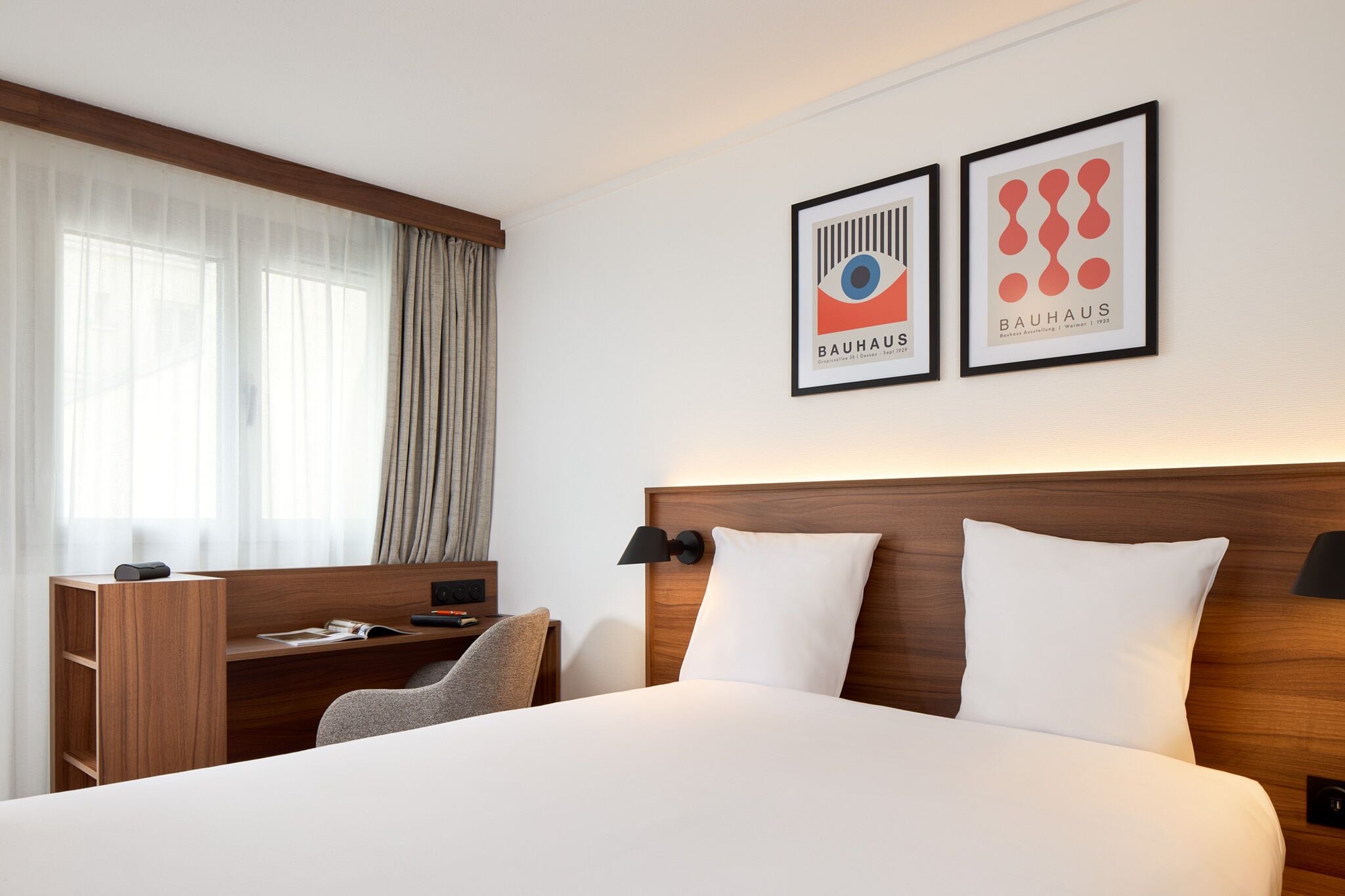 Une chambre d’hôtel avec un lit, un bureau et deux tableaux encadrés au mur.