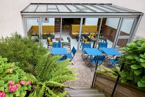 Une terrasse avec des sièges extérieurs, une véranda et un jardin agrémenté de fougères et de fleurs.