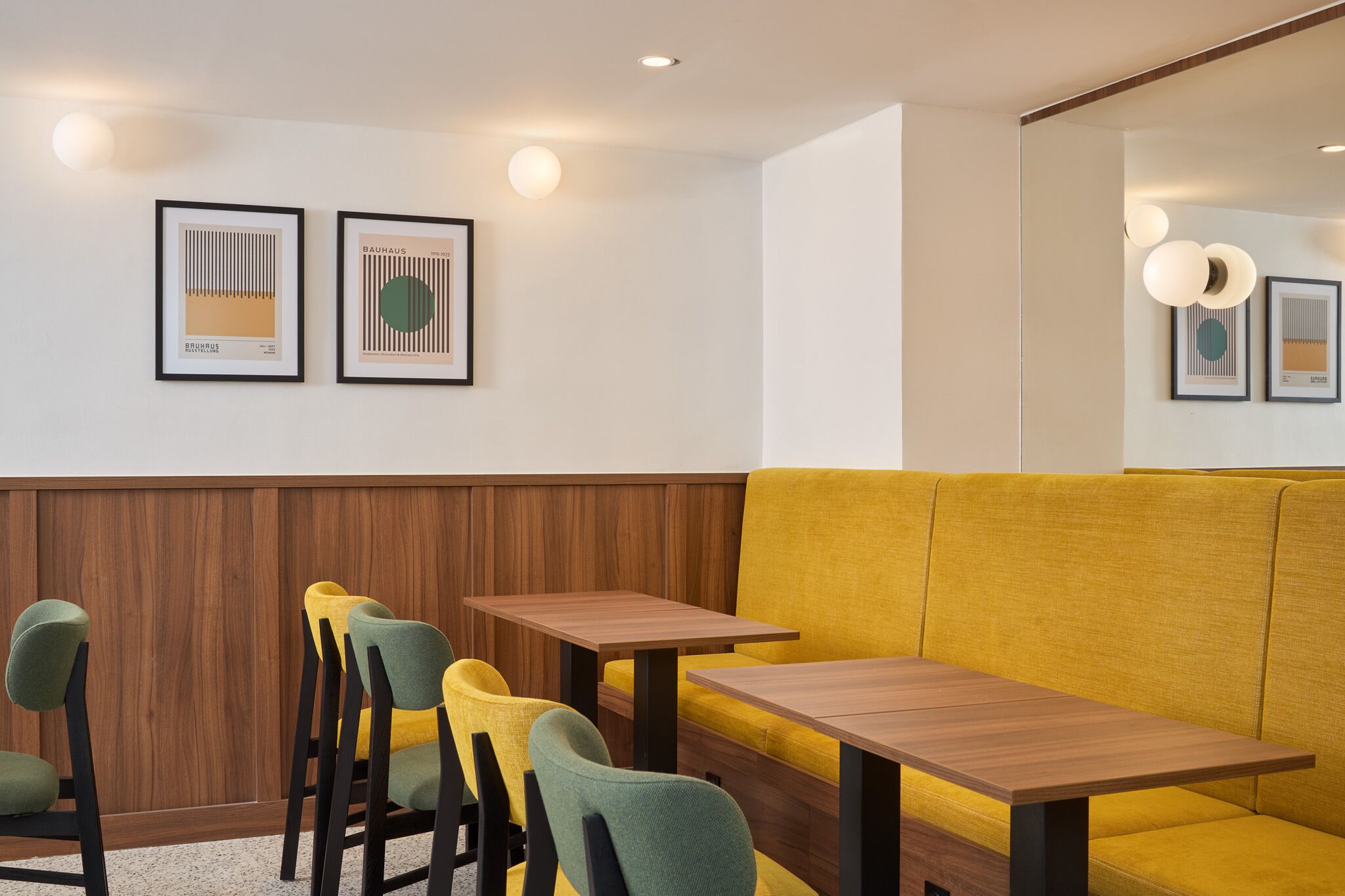 A restaurant interior with wooden paneling, yellow upholstered seating, and framed artwork on the walls.