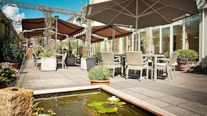 An outdoor patio area with seating, a small pond with lily pads, and umbrellas. - Best Western Hotel President (Bonn)
