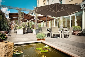 An outdoor patio area with seating, a small pond with lily pads, and umbrellas.