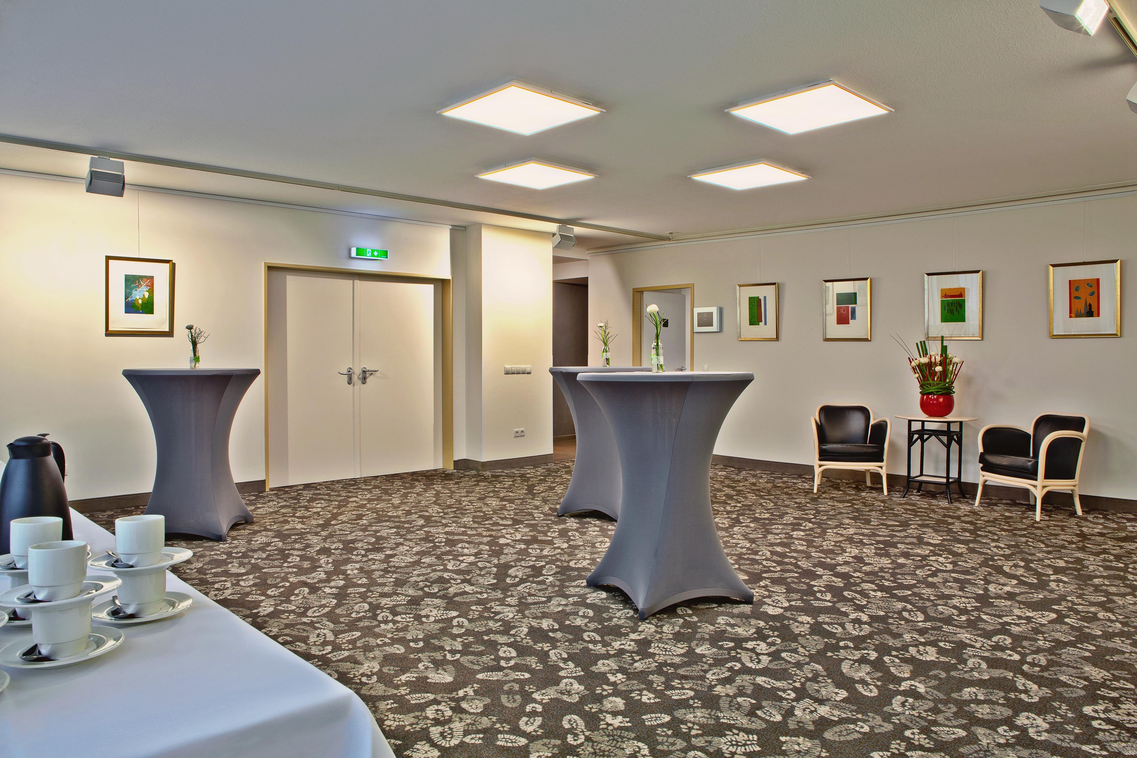 Une chambre d’hôtel avec un sol recouvert de moquette, une table avec des tasses et une bouilloire, et des tableaux encadrés accrochés au mur.