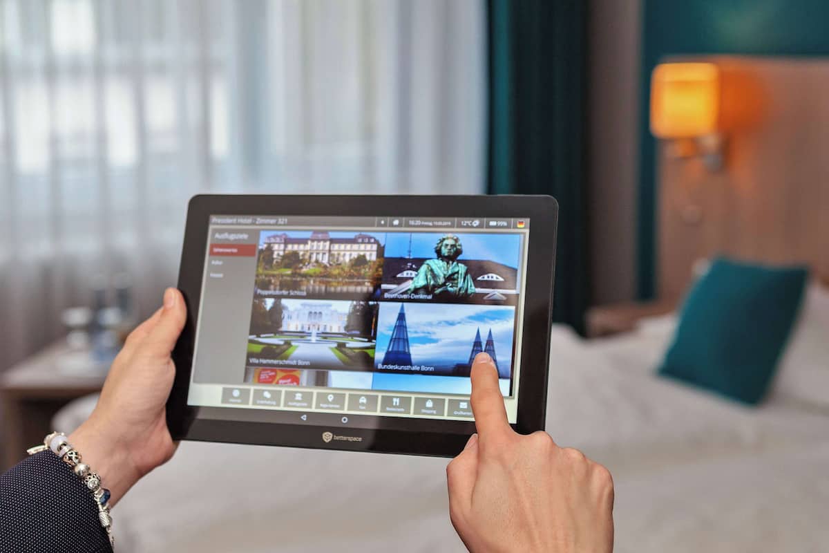 Une tablette affiche une interface de réservation d’hôtel, avec plusieurs chambres et différents équipements visibles.