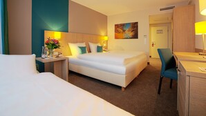 Una habitación de hotel con cama, escritorio, silla, mesita de noche, lámpara y un cuadro en la pared.