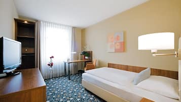 A hotel room with a bed, a desk with a computer, a television, and a window with curtains.