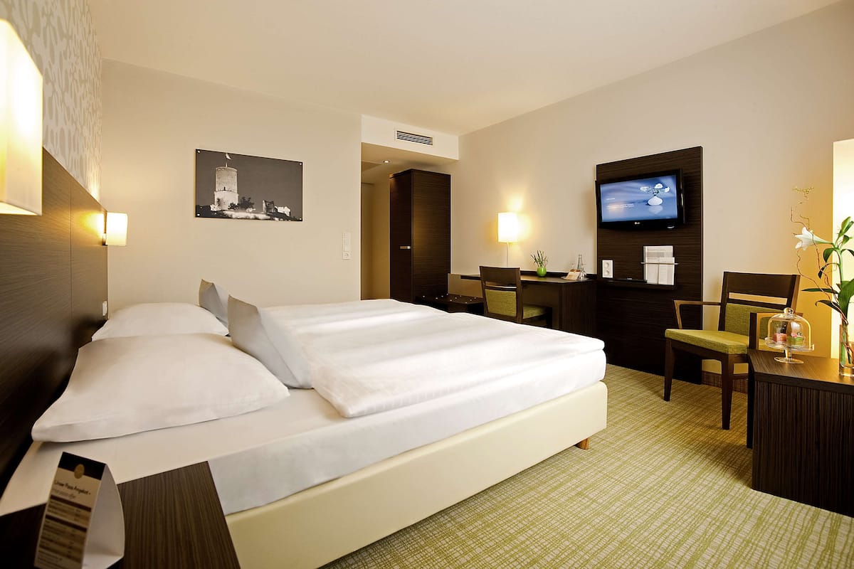 Une chambre d’hôtel avec un grand lit, un bureau avec une chaise, une télévision et un climatiseur fixé au mur.