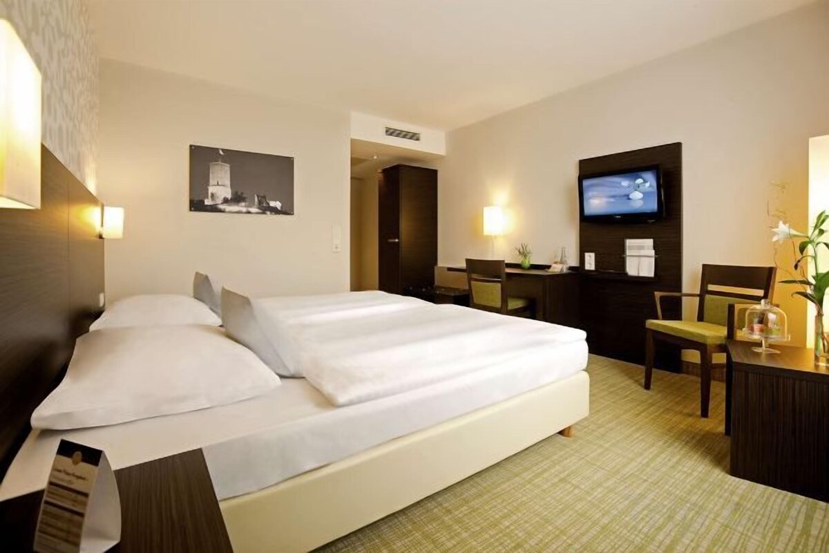 A hotel room with a bed, a desk, a television, and a chair.