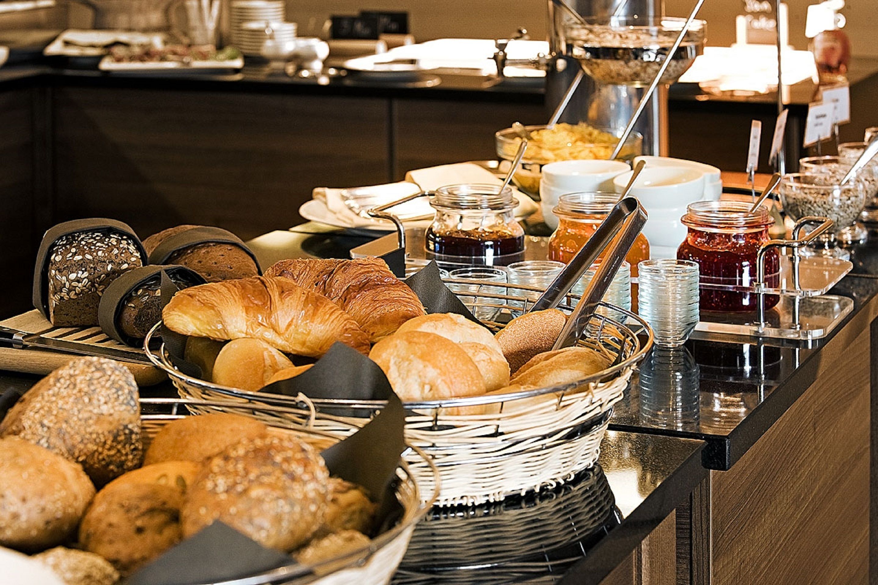A buffet with various breads, pastries, and condiments.