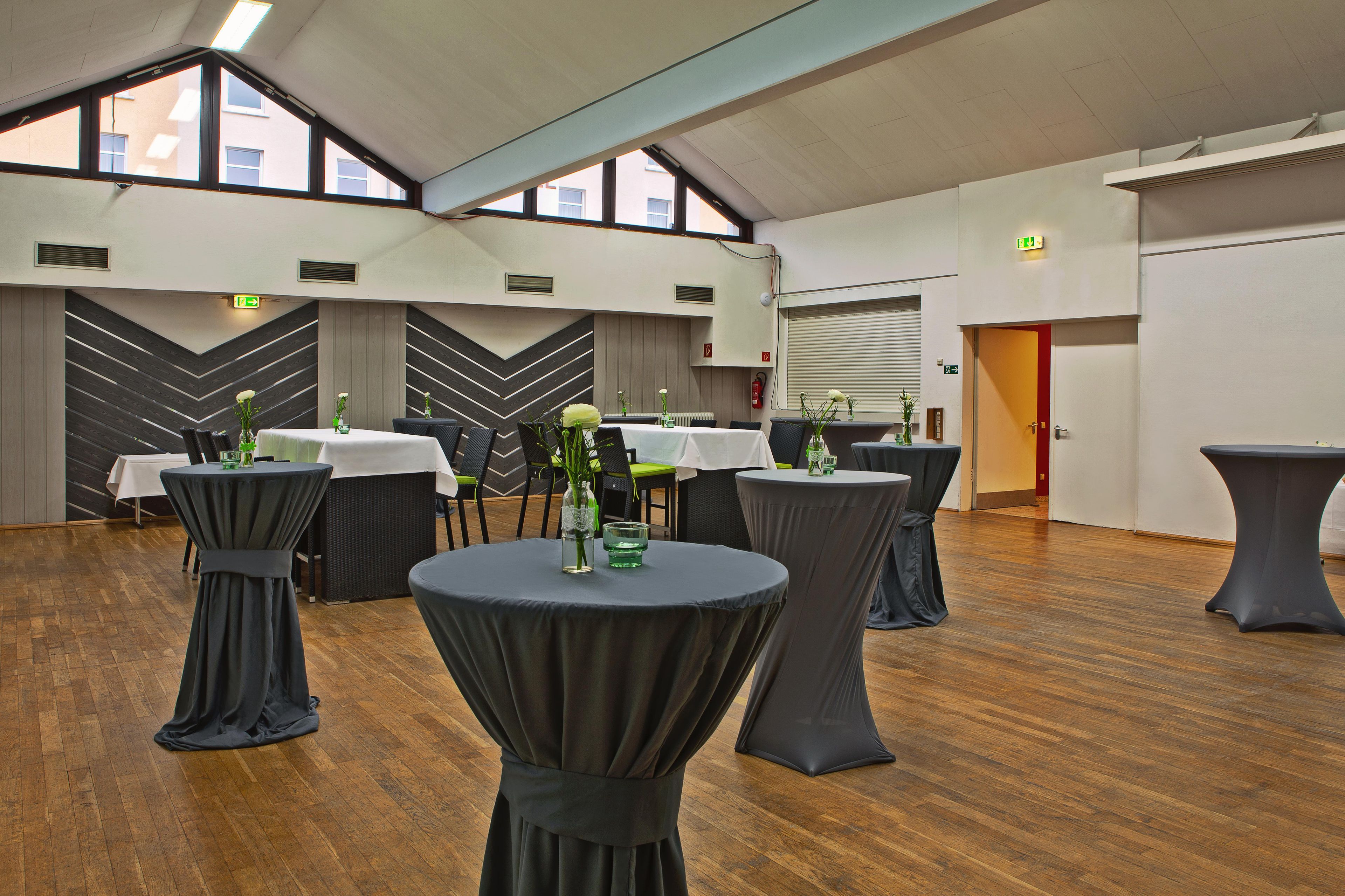 A spacious indoor area with multiple round tables, some with chairs, and a high ceiling with skylights.