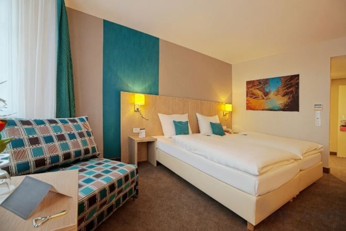 A hotel room with a bed, bedside tables, a desk, and a chair.