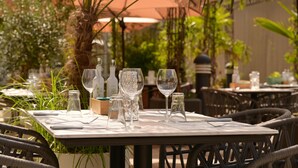 An outdoor dining area with tables set for two, featuring clear glassware and cutlery.