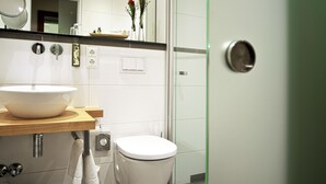 Un baño moderno con un espejo grande, un tocador de madera, un lavabo blanco, un inodoro y una zona de ducha.