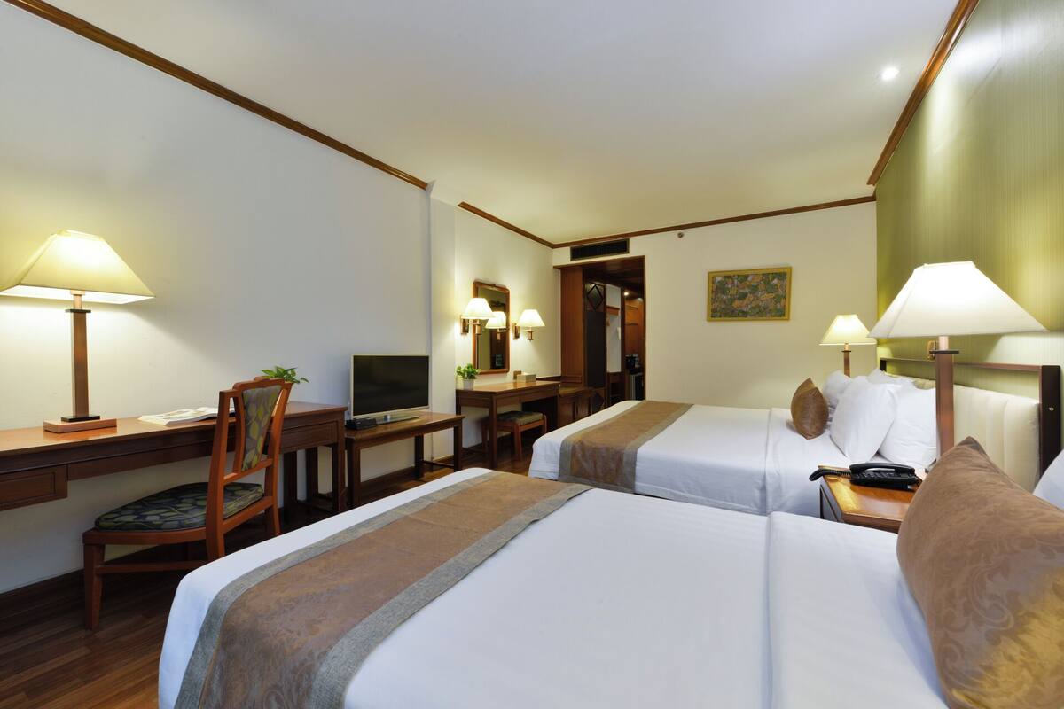 Een hotelkamer met twee bedden, een bureau met een computer, een stoel en twee lampen.