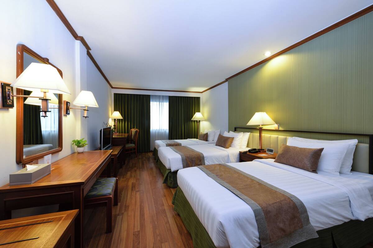 Een hotelkamer met twee bedden, een bureau, een stoel, een spiegel en een raam met gordijnen.