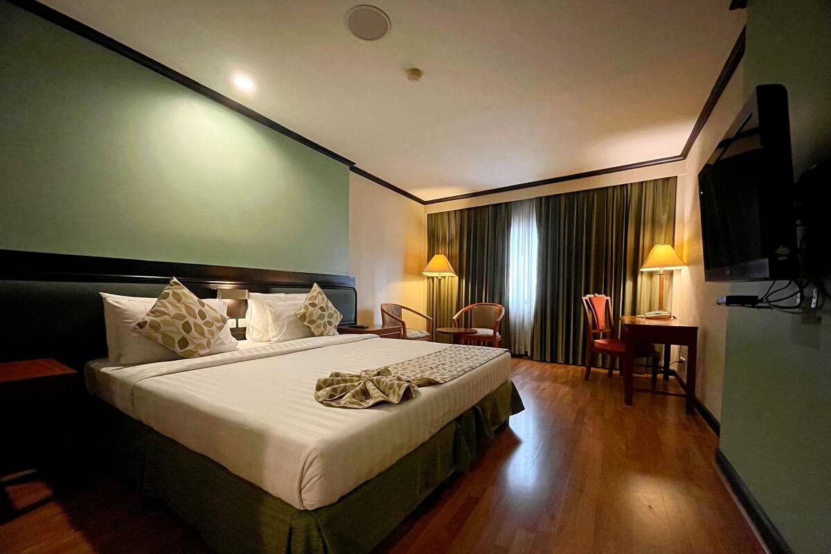 Een hotelkamer met een groot bed, een bureau, twee stoelen, een televisie en een raam met gordijnen.