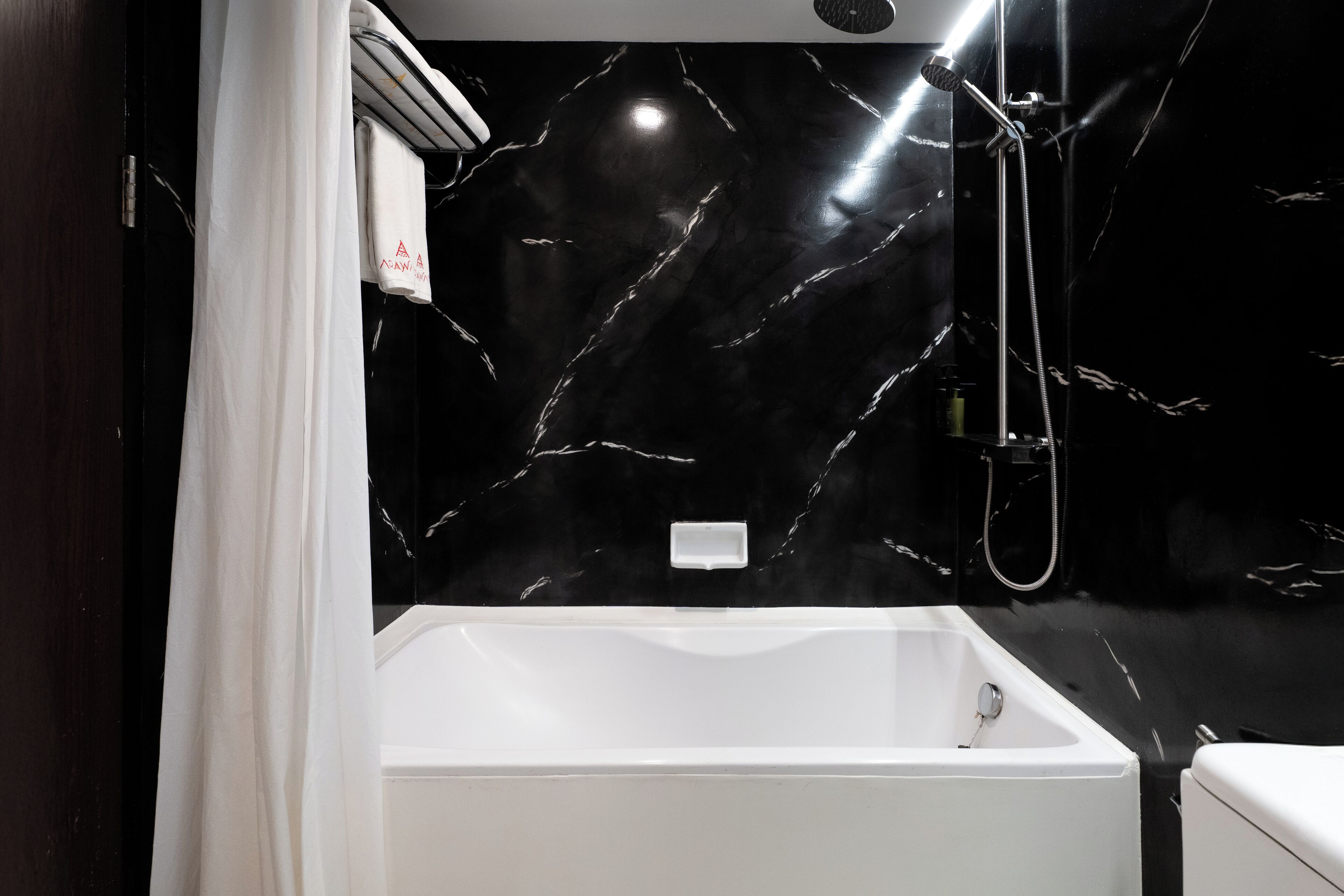 Une salle de bain moderne avec une baignoire blanche, une douche et un mur en marbre noir.