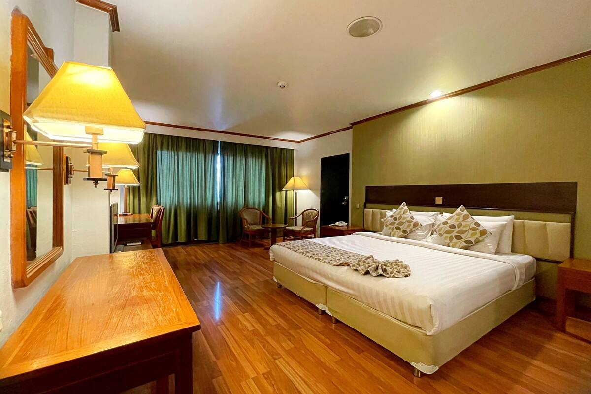 Een hotelkamer met een groot bed, een bureau, een stoel, een lamp en een gordijn.