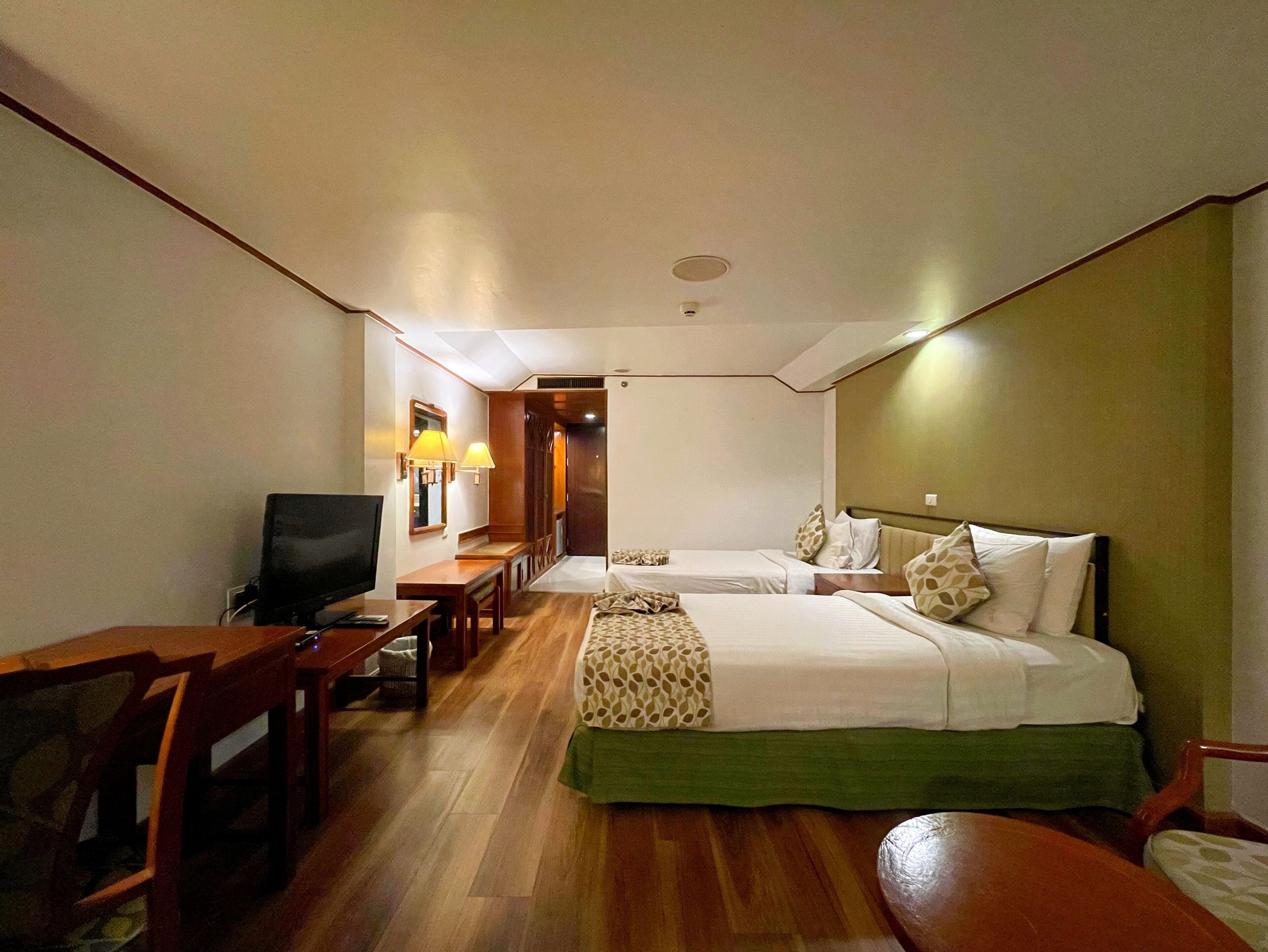 A hotel room with two beds, a desk, a chair, and a television.