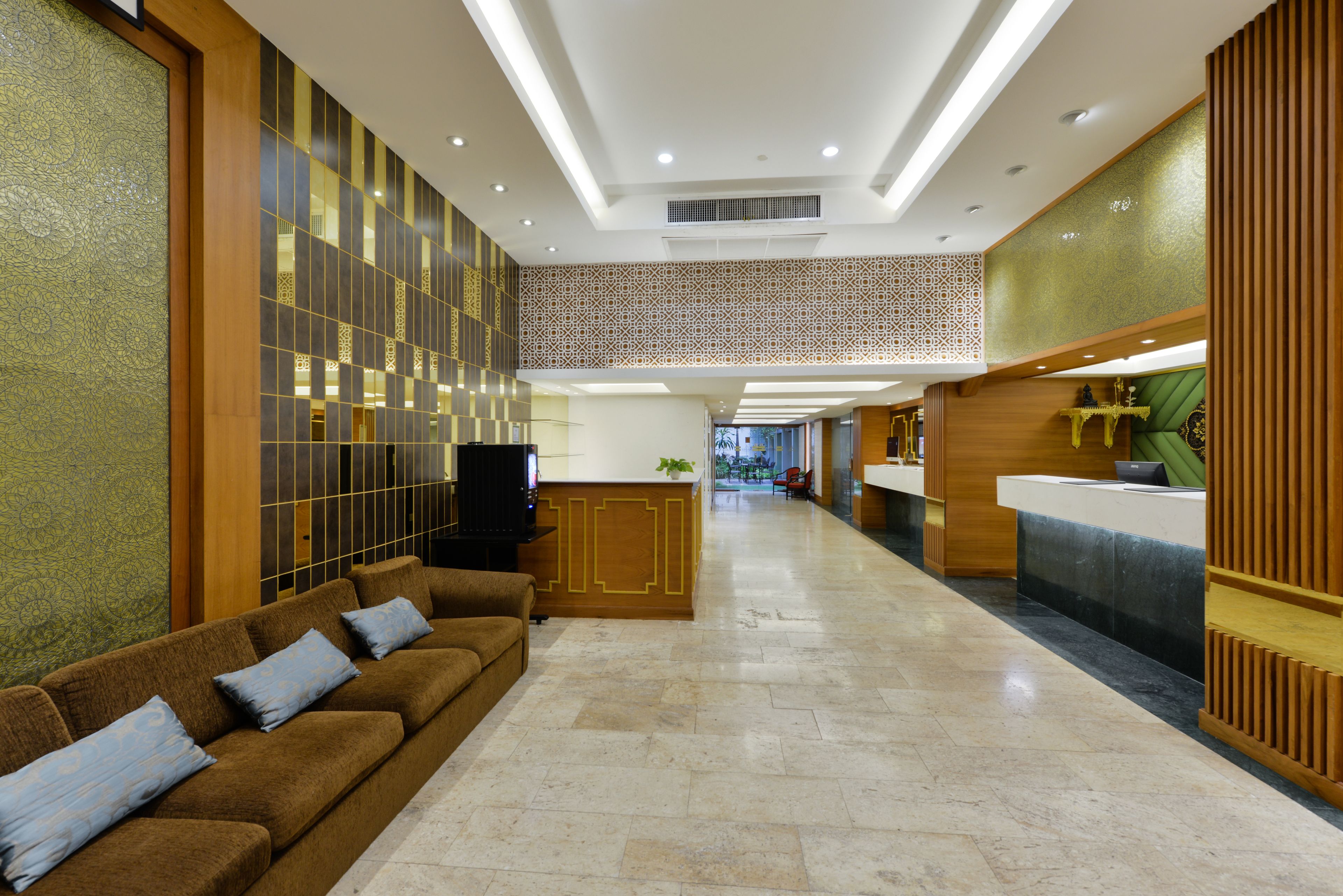 Una hall d'albergo con una reception, un'area salotto con divano e poltrone, e una parete decorata.