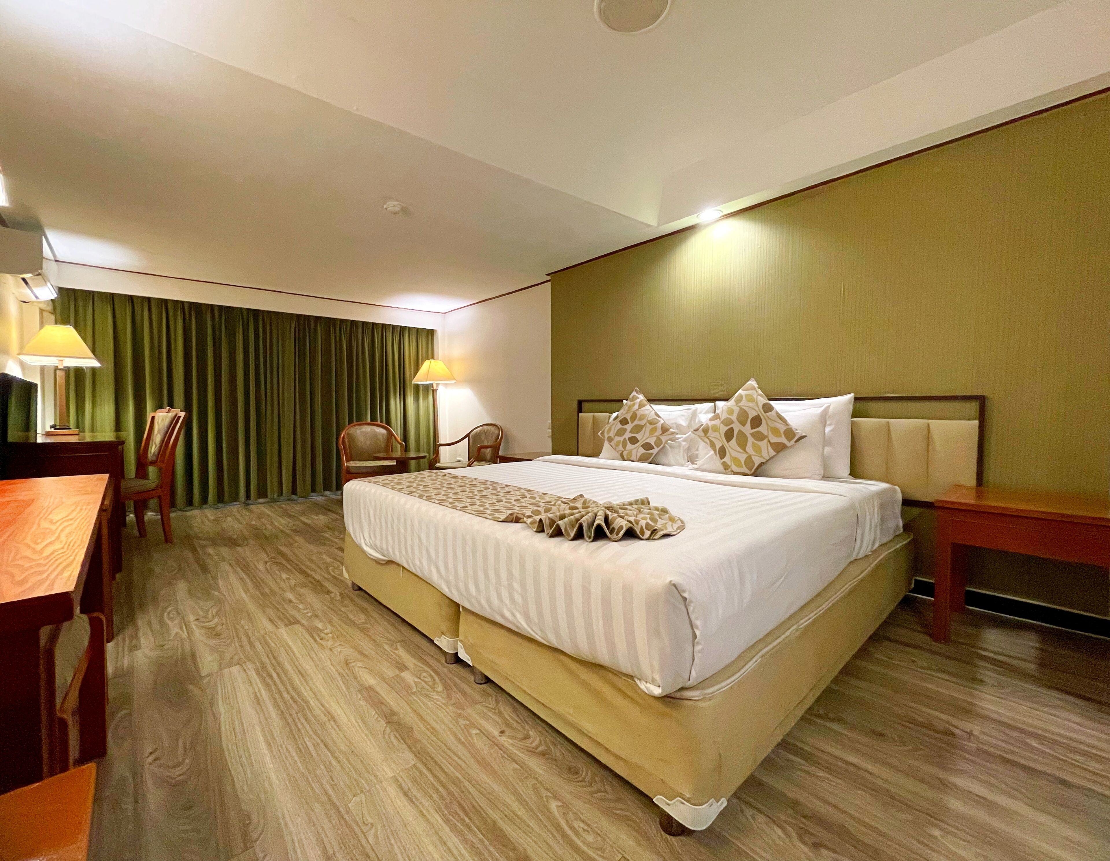 A hotel room with a large bed, two chairs, a desk, and a lamp.