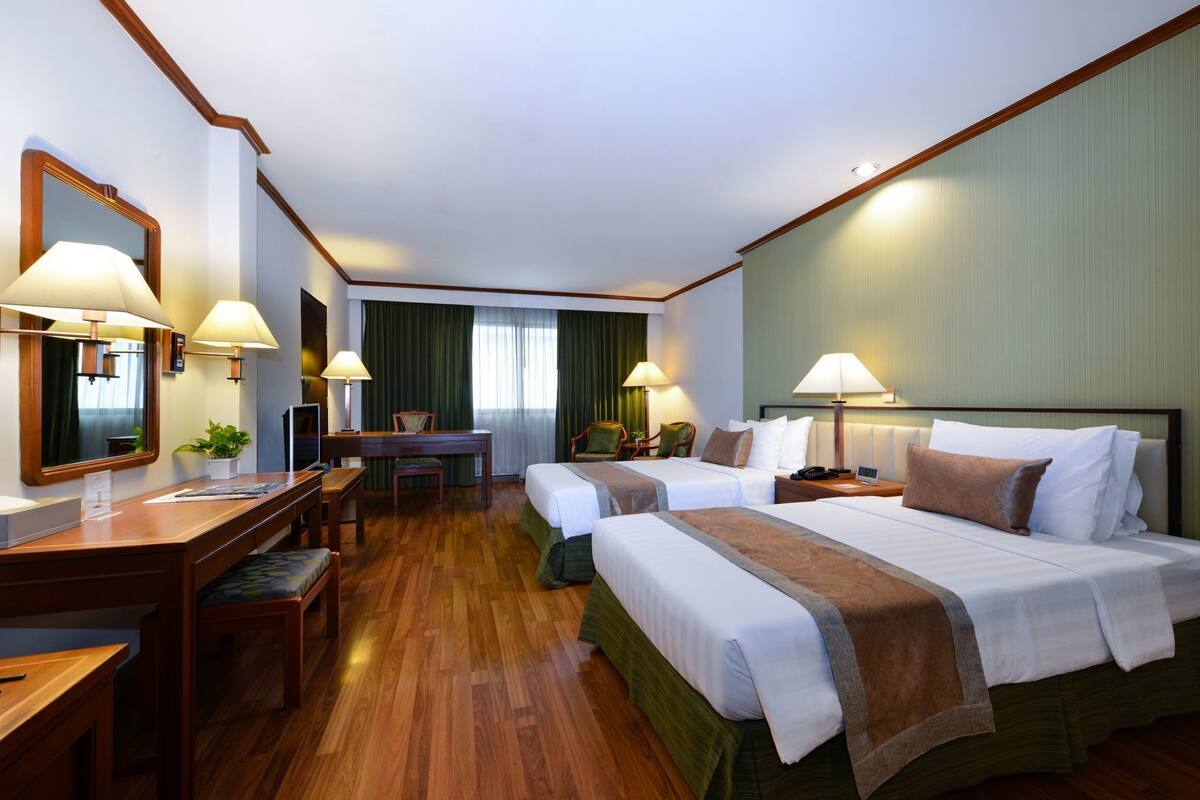 Een hotelkamer met twee bedden, een bureau, een stoel, een spiegel en een raam met gordijnen.