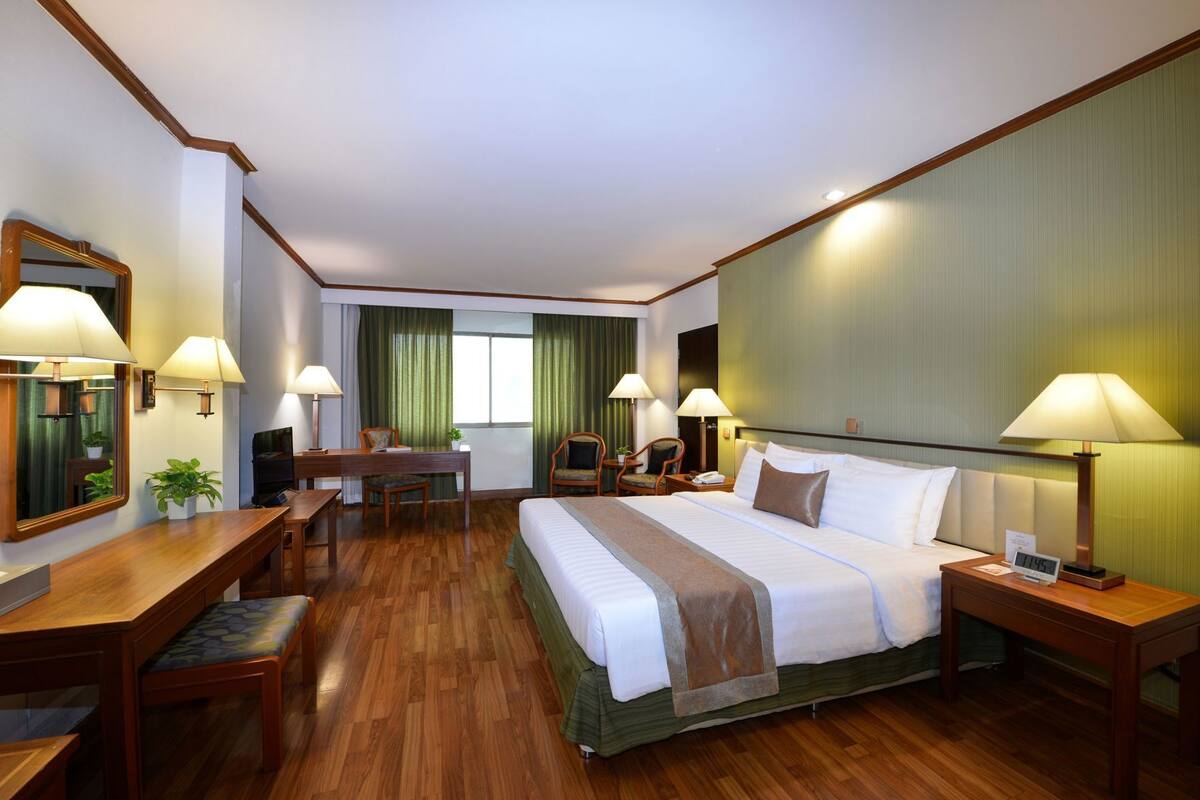 Een hotelkamer met een groot bed, een bureau, twee stoelen, een televisie en een wekker op het nachtkastje.