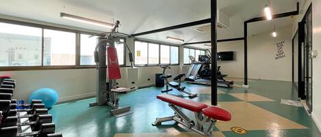 Un gimnasio con equipamiento de ejercicio, una banca y una pared con mensajes motivacionales.