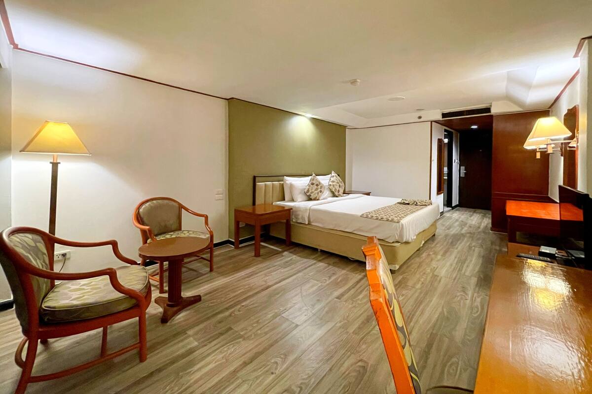 Een hotelkamer met een bed, twee stoelen, een klein tafeltje en een bureau met een lamp.