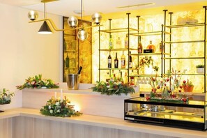 A bar area with shelves of bottles, a cash register, and decorative floral arrangements.