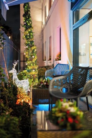Een versierde buitenruimte met een kerstboom, rieten stoelen en een witte rendierdecoratie.