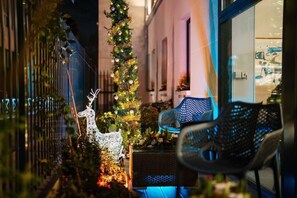 A narrow outdoor corridor with a Christmas tree, a white reindeer decoration, and a chair.