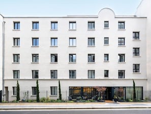 Een hotel met meerdere verdiepingen, een symmetrische gevel, gelijkmatig verdeelde ramen en een hek met terrasplaatsen.