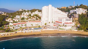 Un hotel frente al mar con varias construcciones, una playa y una zona de piscina.