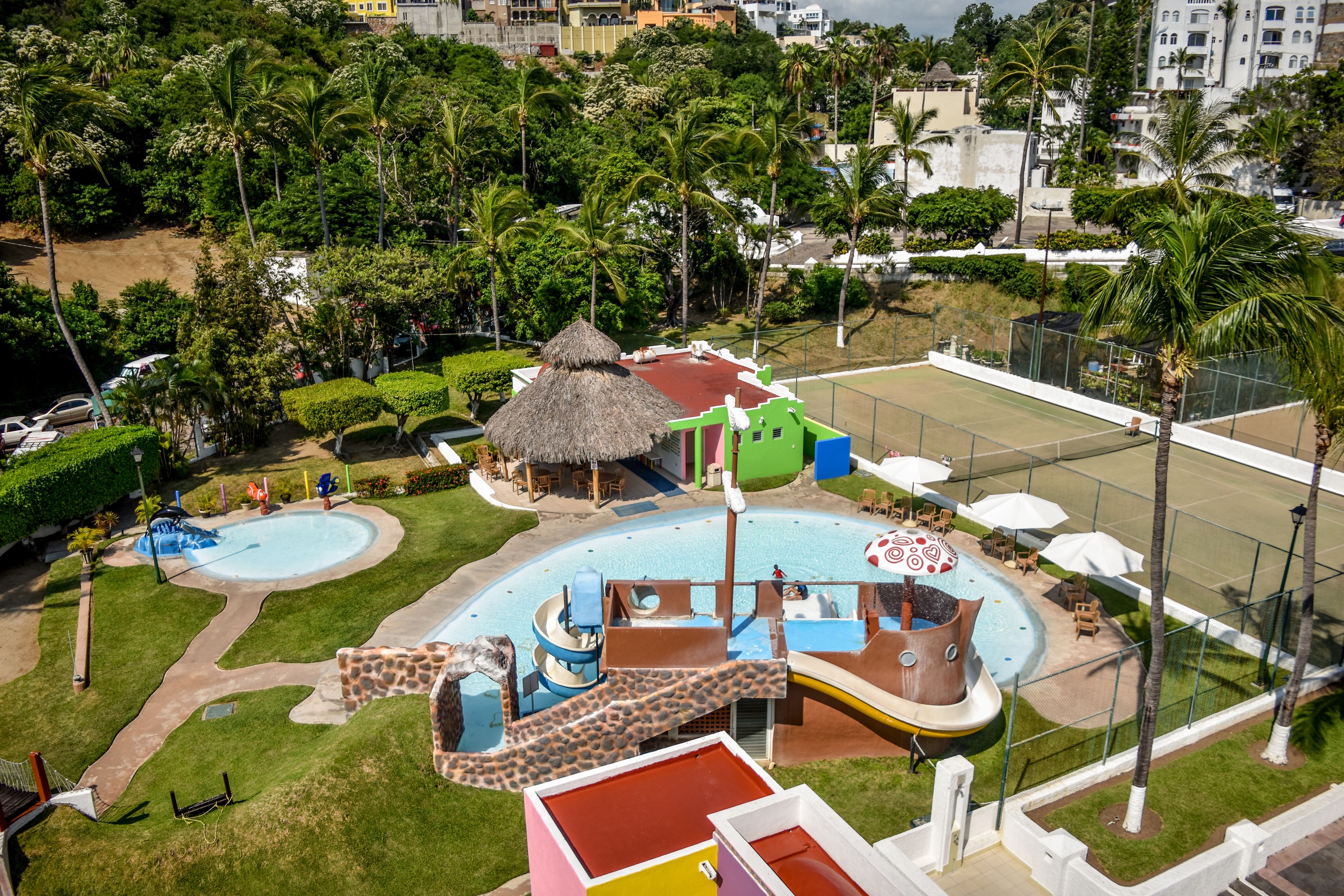 A resort with multiple swimming pools, a slide, and a thatched-roof hut.